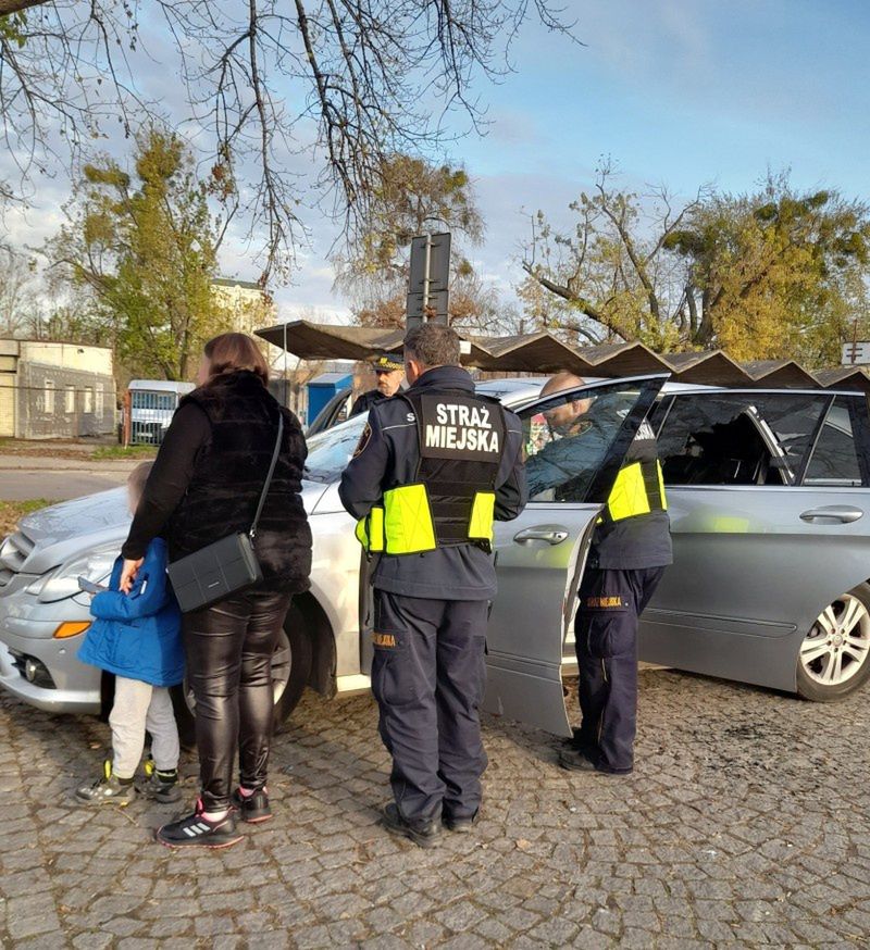 Strażnicy miejscy, kobieta i dziecko przy samochodzie