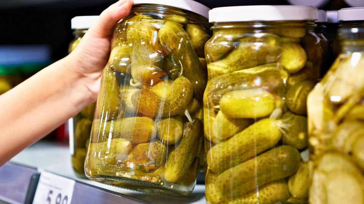 Kobieta sięga po słoik ogórków w sklepie