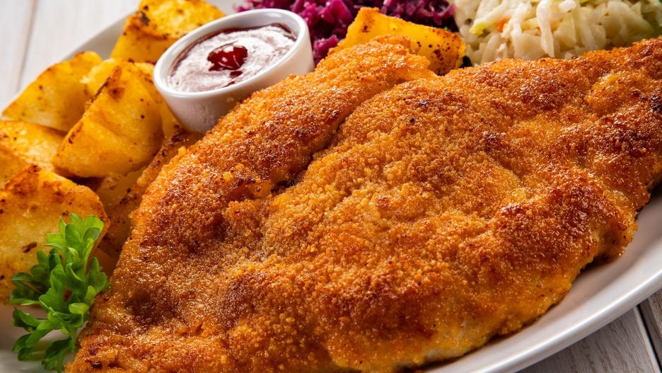 Breaded fried pork chop with boiled potatoes and cabbage salad on wooden table