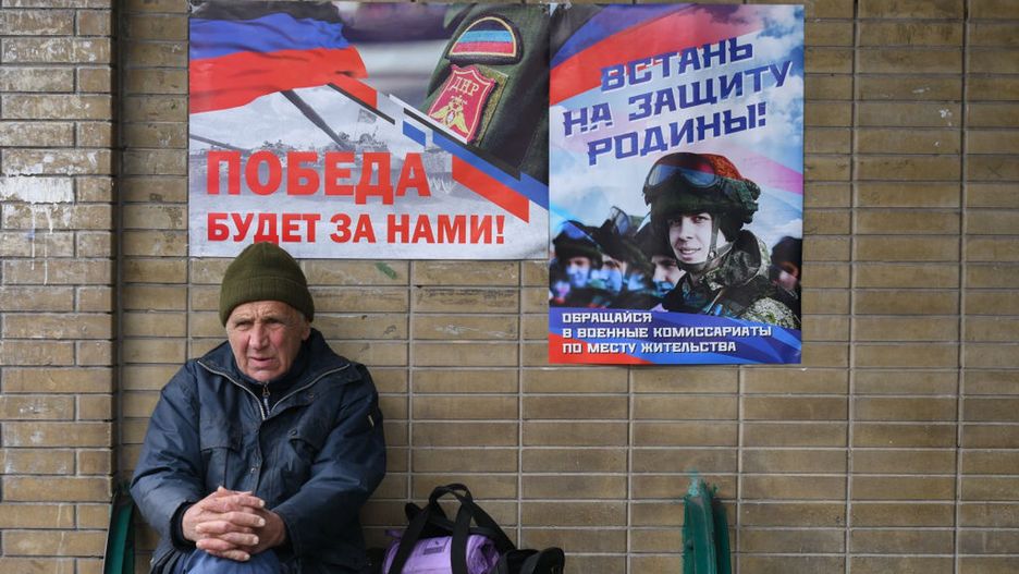 Mieszkaniec Doniecka siedzi pod plakatami propagandowymi armii rosyjskie