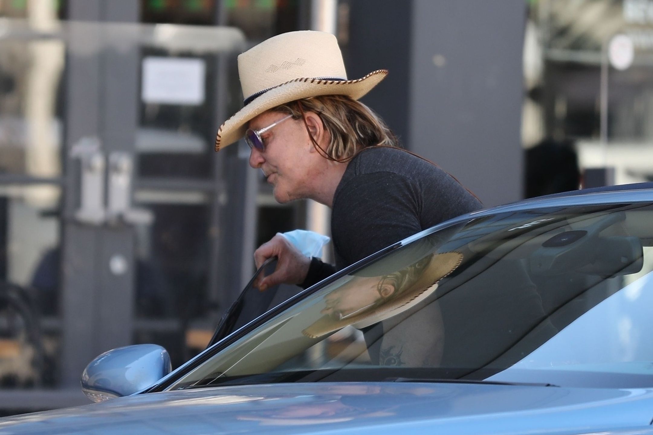 Zmarnowany Mickey Rourke wyłania się z samochodu w kowbojskim kapeluszu 