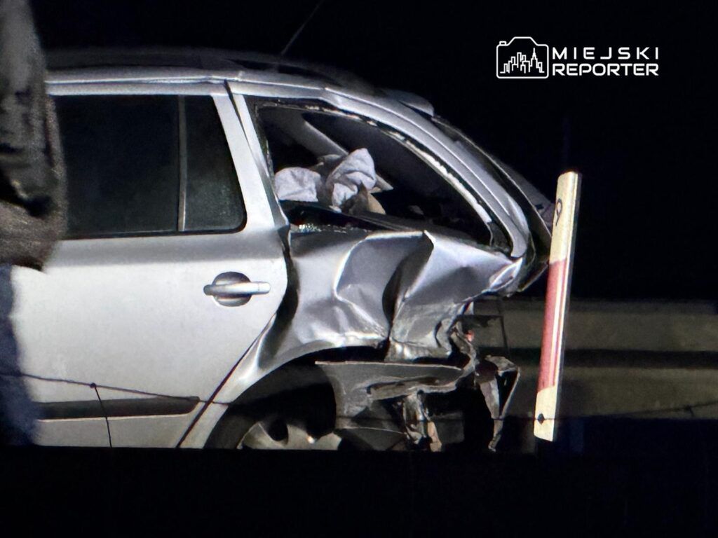 Uszkodzony samochód osobowy z wgniecioną tylną częścią, zaparkowany w ciemnej okolicy.