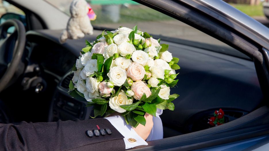 Pan młody siedzi w samochodzie trzymając bukiet dla panny młodej