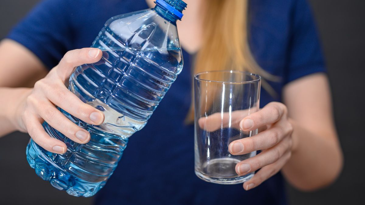 Kobieta nalewająca wodę do szklanki z plastikowej butelki 