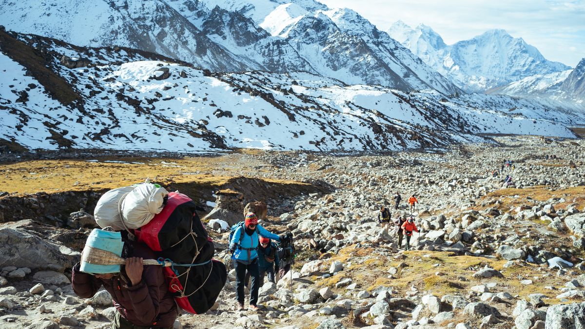 GORAKSEHP, NEPAL - OCTOBER 12: Porters, trekkers and guides make their way to Gorakshep with the Khumbu glacier in the background on October 12, 2024 in Gorakshep, Sagarmatha Region, Nepal. The growing popularity of trekking in Nepal has resulted in various forms of pollution spoiling the fragile ecosystem. Gorakshep is the last human settlement on the Nepal side before trekkers arrive at Everest Base Camp just 3.5km away. Here, waste management issues due to trekking tourism are apparent with plastic bottles and debris from lodges and restaurants dumped just meters from the town centre. Early in the autumn trekking season, Everest Base Camp itself also shows signs of waste mismanagement. (Photo by Mailee Osten-Tan/Getty Images)