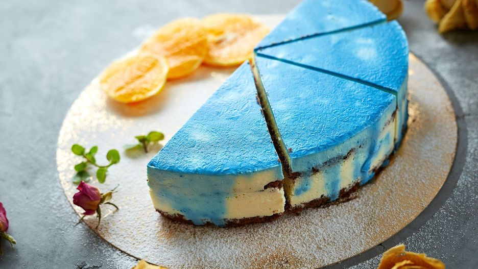 half of cutted mousse cake with blue glaze on a dark gray concrete background