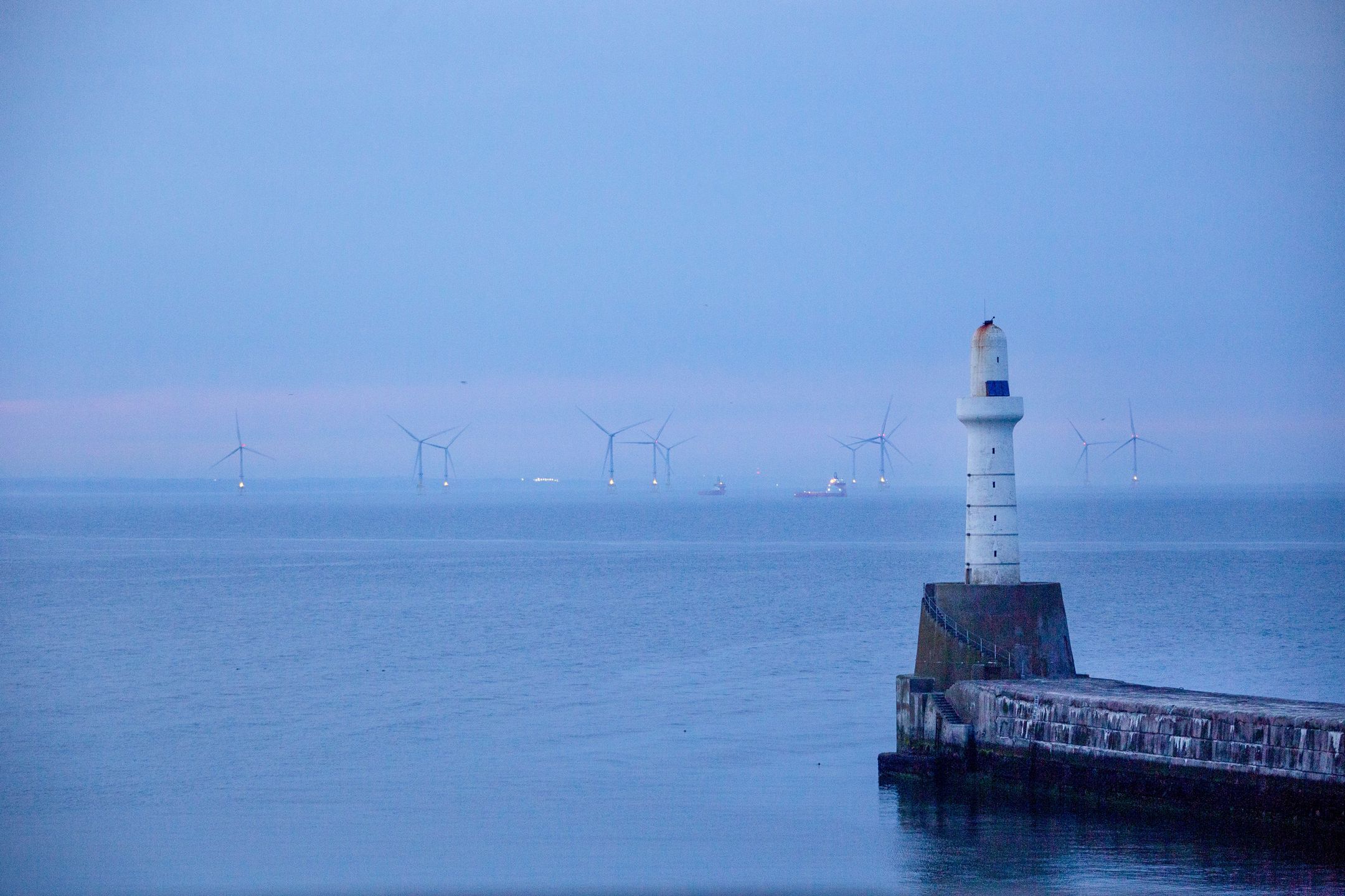 Offshore wind turbines beyond the harbour arm at the Port of Aberdeen sea port at dusk in Aberdeen, UK, on Monday, July 18, 2022. Aberdeen in northeast Scotland is trying to make the leap from an oil town to a renewables hub amid growing demand for cheap home-grown energy. Photographer: Emily Macinnes/Bloomberg via Getty Images