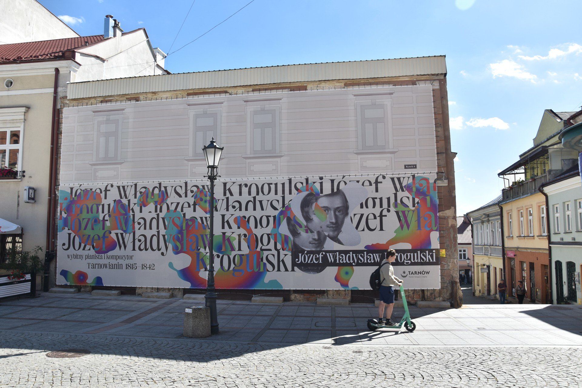 Wielkoformatowy wydruk, który zasłonił spaloną kamienicę od strony Rynku, składa się z dwóch części. Dolna dedykowana jest Józefowi Władysławowi Krogulskiemu