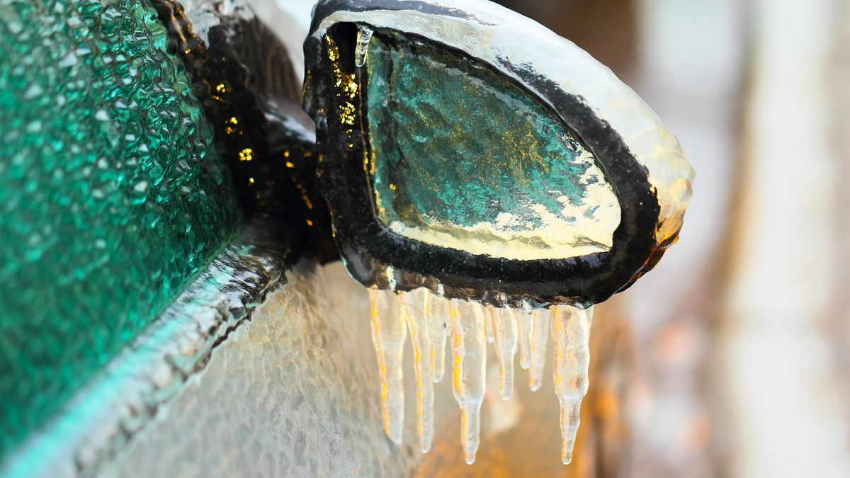 Car side mirror covered with ice and icicles, close up