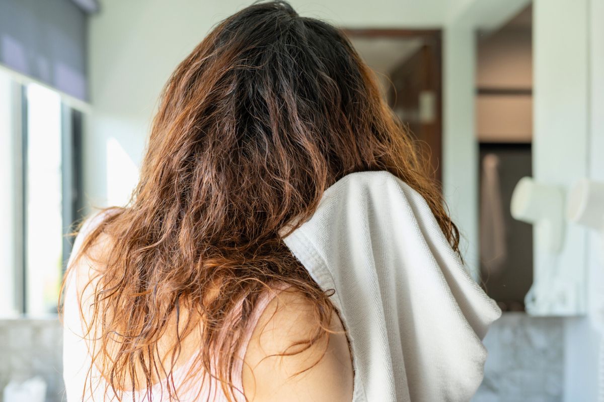 The woman is drying her hair with a towel.