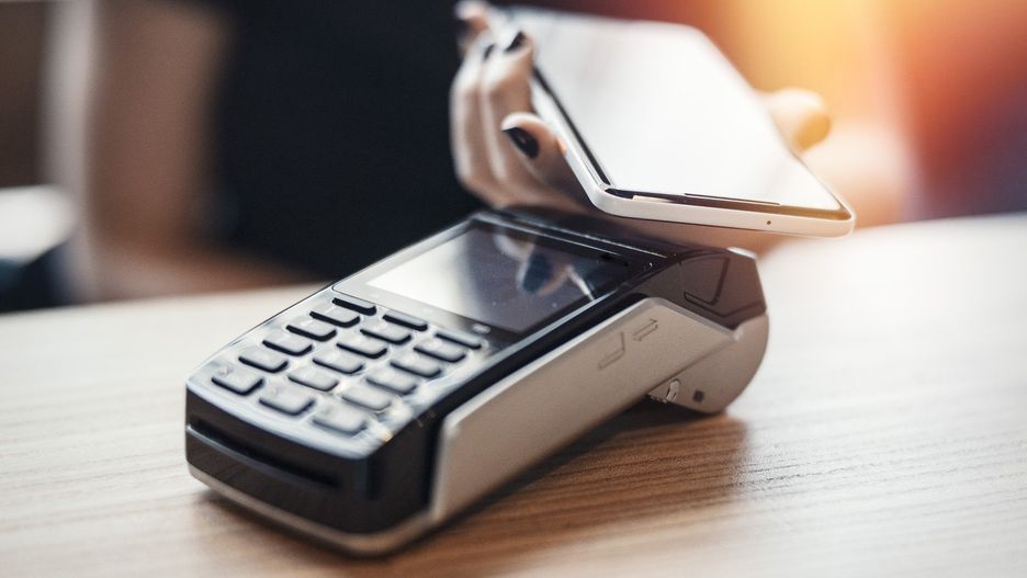 Young woman pays via payment terminal and mobile phone.