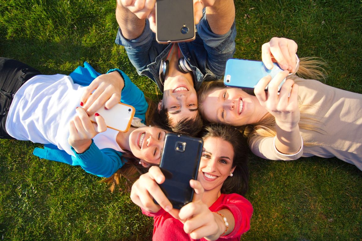 Outdoor portrait of group of friends taking photos with a smartphone in the park