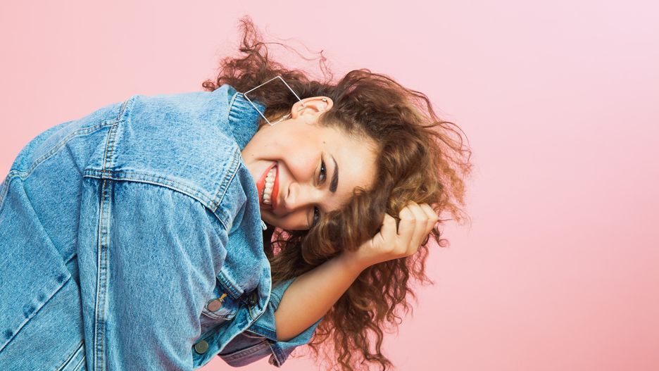 Beautiful young woman with curly hair in denim clothes. Trendy look, positive emitions, smile, copy space