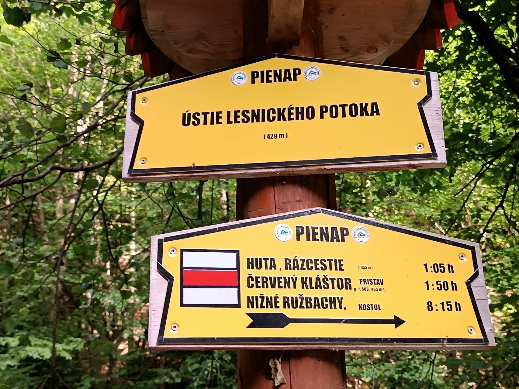 Żółty słowacki drogowskaz Ústie Lesnického potoka z kierunkiem Huta i Červený Kláštor oraz czerwonym oznaczeniem szlaku