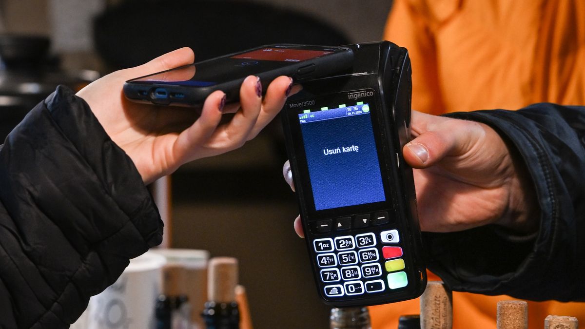 KRAKOW, POLAND - NOVEMBER 29:   A lady pays for her wine purchase with her mobile phone at the Christmas Market in Krakow's UNESCO-listed Market Square, with festive stalls and holiday decorations in the historic Old Town, on November 29, 2024 in Krakow, Poland. (Photo by Artur Widak/NurPhoto via Getty Images)