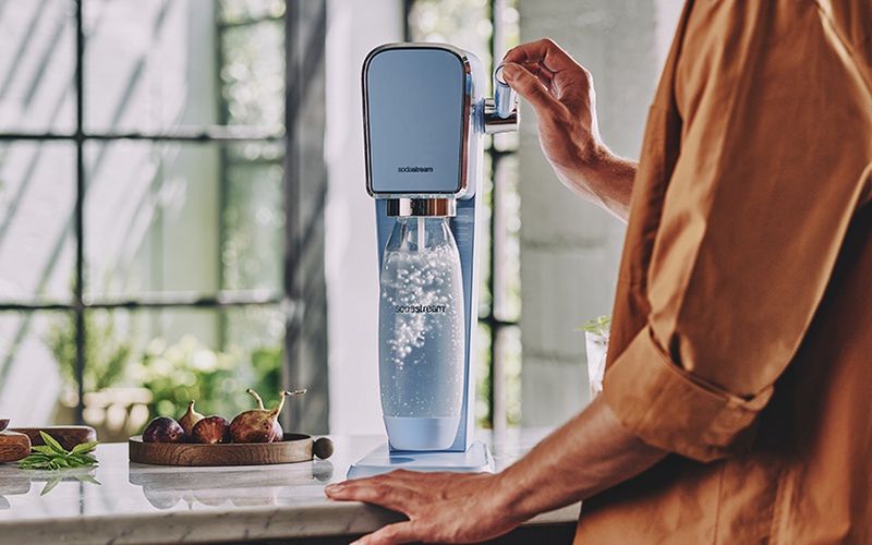 Mężczyzna robiący wodę gazowaną w niebieskim saturatorze SodaStream Art - zdjęcie.