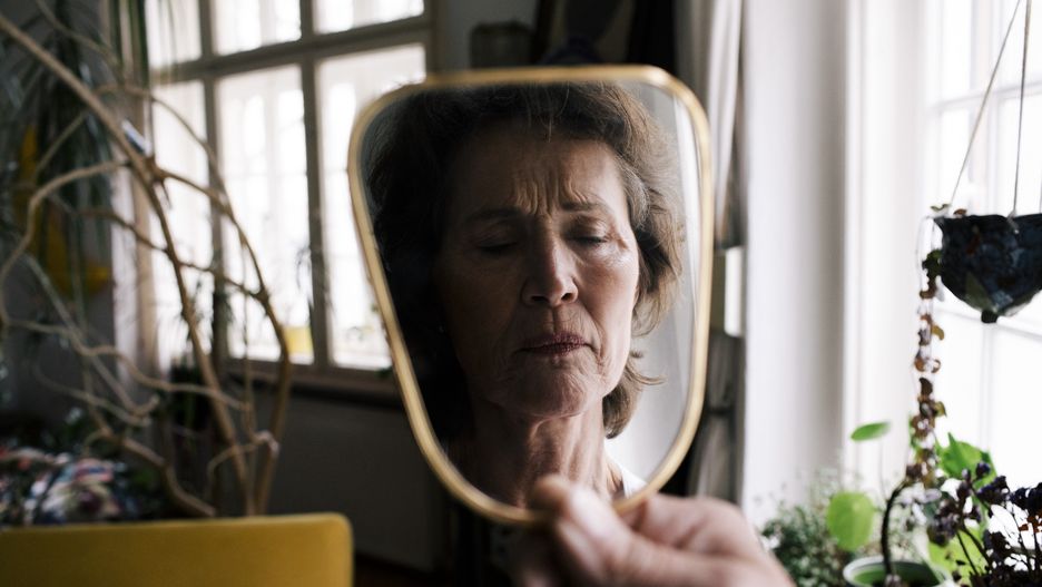 Reflection of upset senior woman on hand mirror at home
Maskot