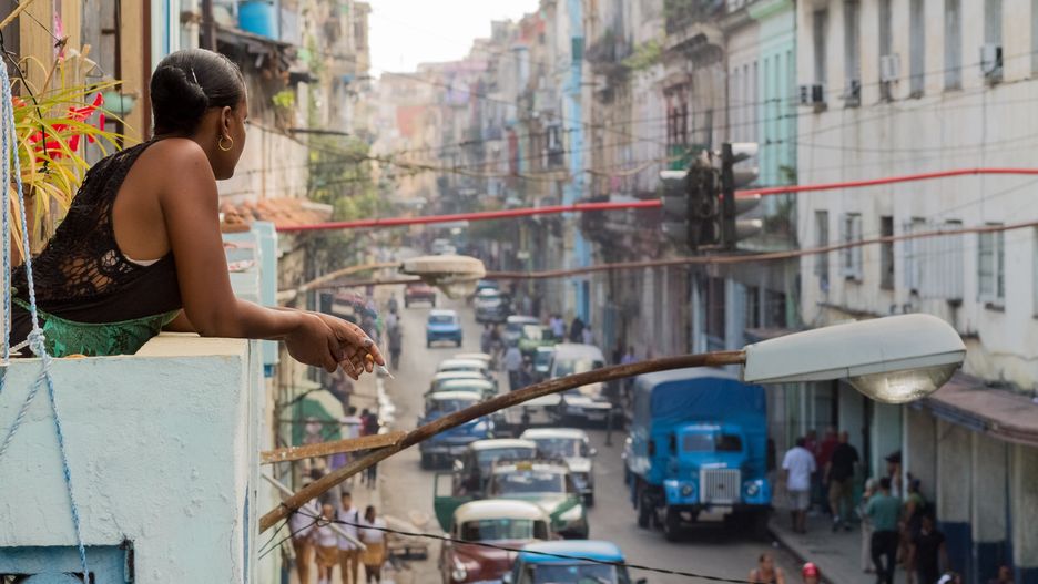 Young woman on a cigarette break at a balcony over viewing a street in Havana.Radu HarangusCuba, Havana, Travel