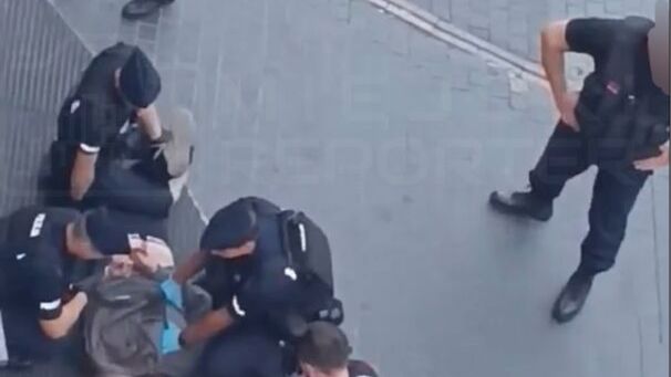 Grupa ratowników i policjantów udziela pomocy osobie leżącej na ziemi w miejskim otoczeniu.