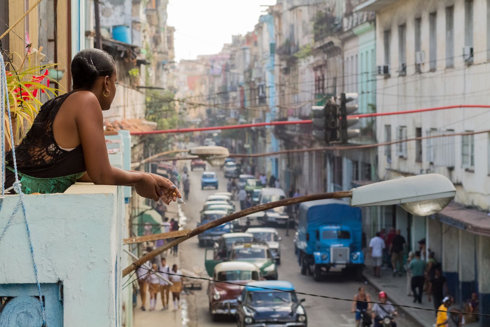 Young woman on a cigarette break at a balcony over viewing a street in Havana.Radu HarangusCuba, Havana, Travel