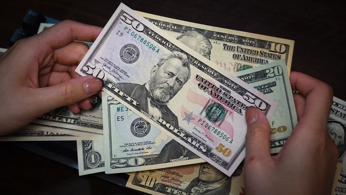 SHANGHAI, CHINA - 2024/08/31: In this illustration, a person is holding some US dollar cash bills in his hands, some of which are placed on a table. (Photo Illustration by Sheldon Cooper/SOPA Images/LightRocket via Getty Images)