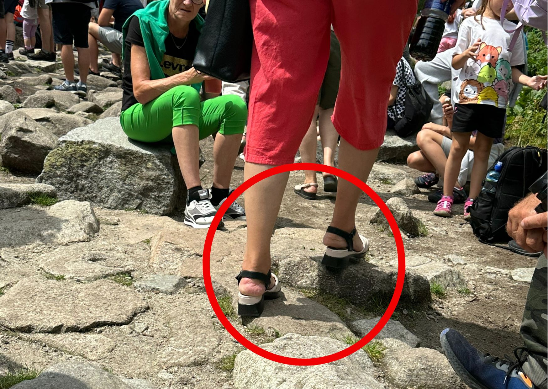 Turyści chodzą w klapakach po kamieniach nad stawem