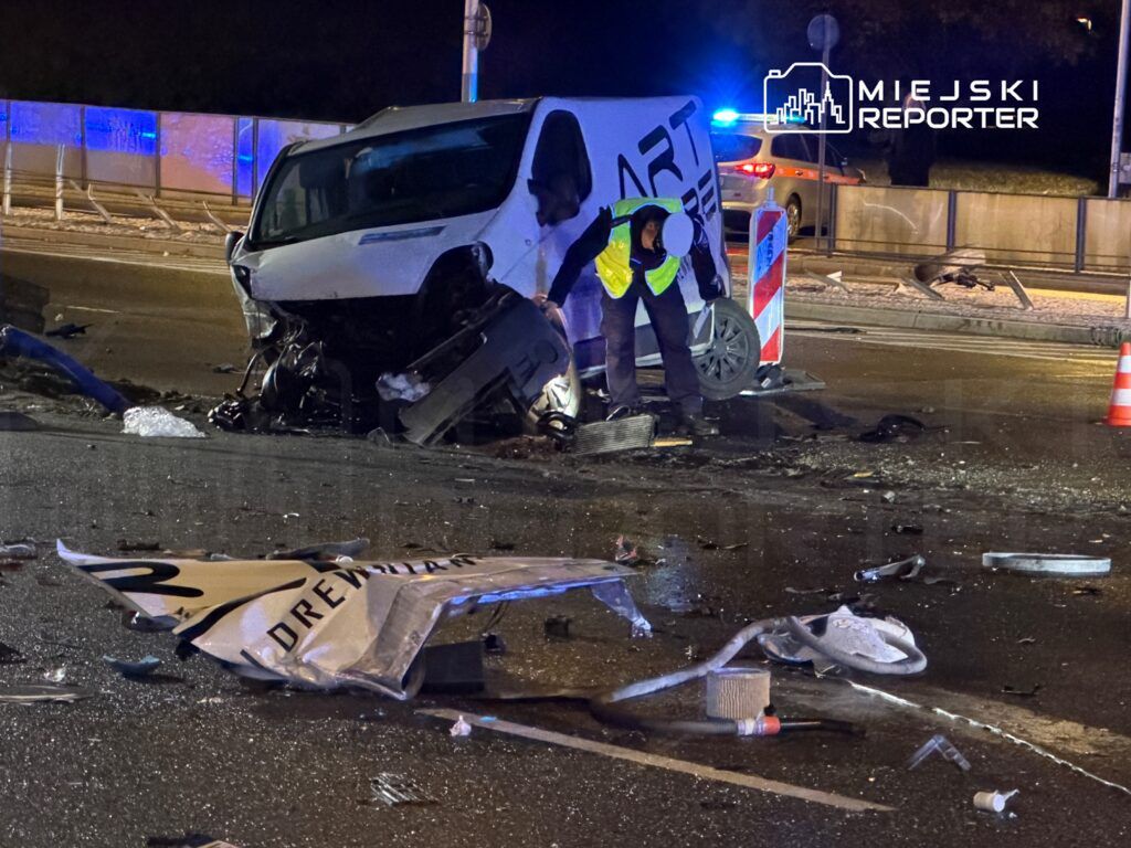 Mężczyzna w kamizelce odblaskowej bada skutki wypadku samochodowego na drodze, obok uszkodzonego pojazdu.