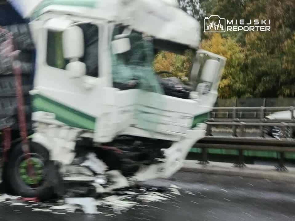 Uszkodzony ciężarowy pojazd leżący na boku na pasie drogowym, otoczony porozrzucanymi przedmiotami.