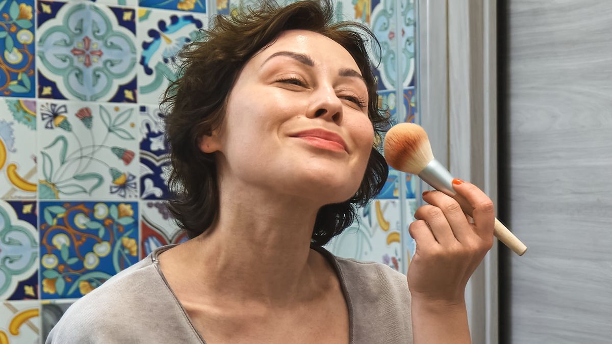 Uśmiechnięta kobieta maluje policzki bronzerem