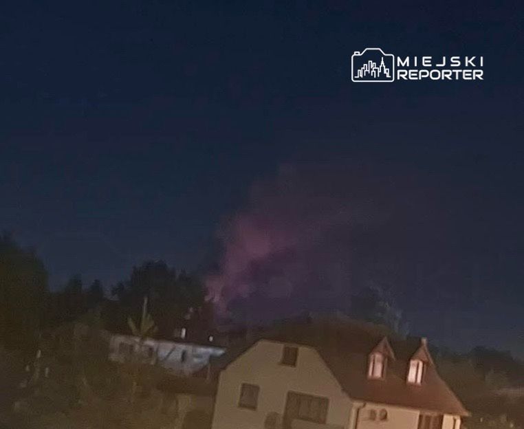 Na niebie widoczny różowy dym, w tle zabudowania mieszkalne w nocy.