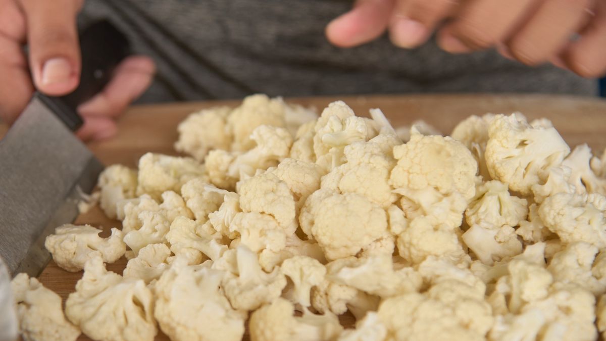 Preparing Cauliflower for Cooking at HomeFresh Cauliflower Being Chopped on Wooden Cutting BoardKrit of Studio OMG