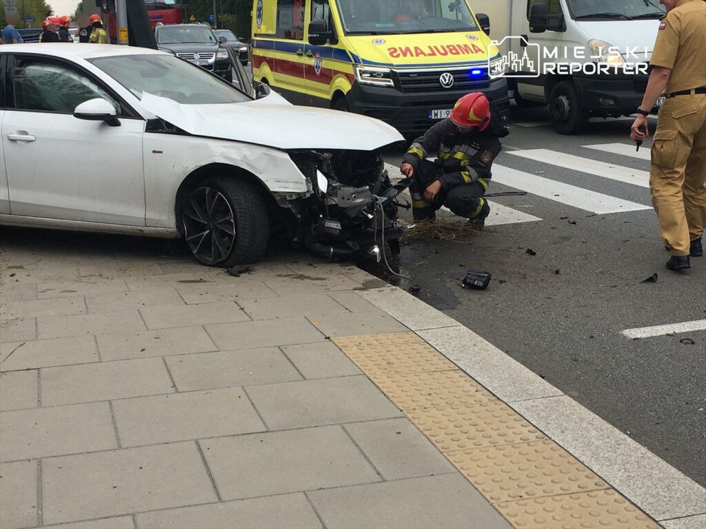 Strażak sprawdzający uszkodzenia białego samochodu osobowego po wypadku drogowym na ulicy w mieście.
