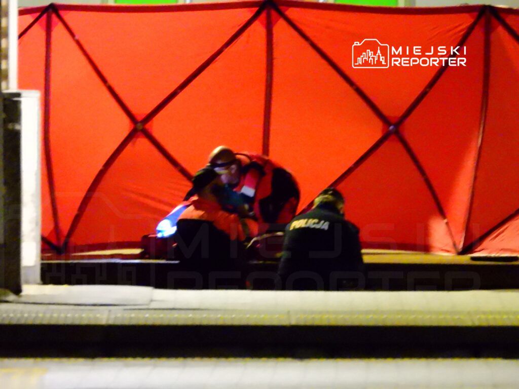 Ratownicy medyczni pomagają osobie w czerwonym namiocie, podczas nocnej interwencji na ulicy.