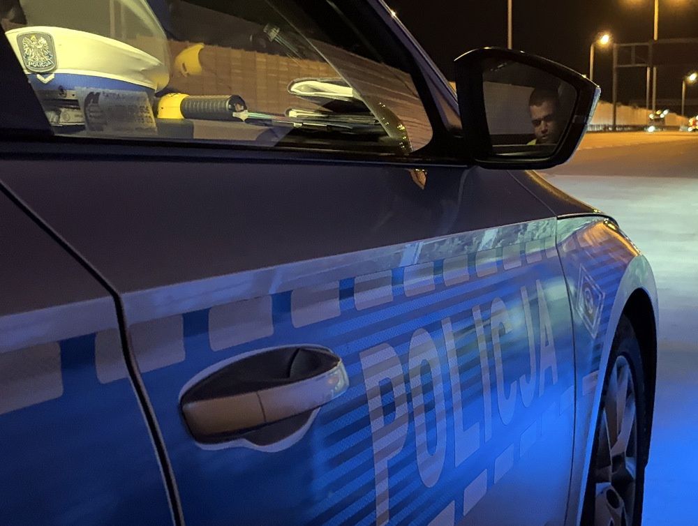 Policyjny samochód zaparkowany na nocnej ulicy, z widocznym napisem "POLICJA" na drzwiach.