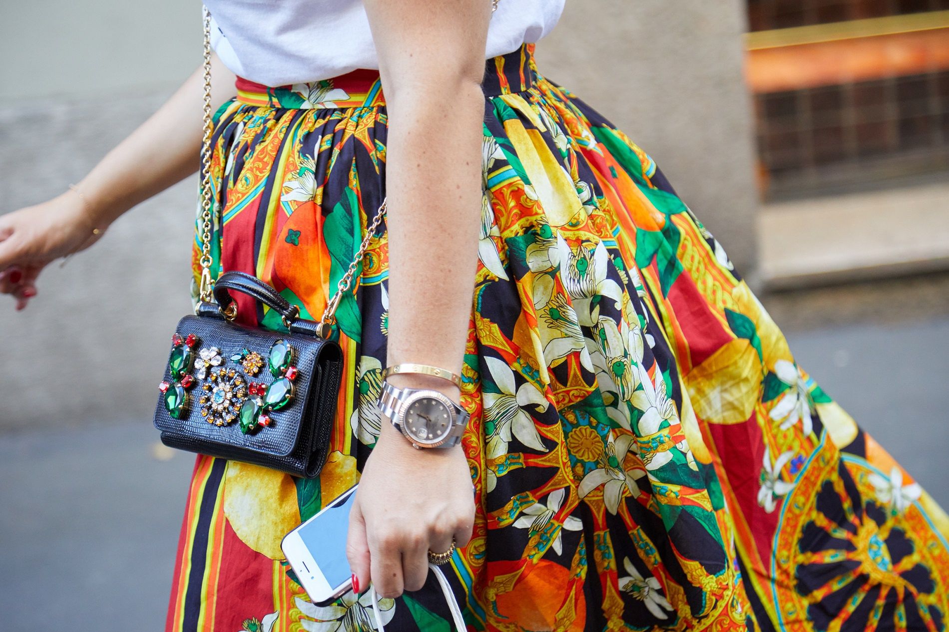 MILAN - JUNE 17: Woman with yellow, red and orange floral skirt, jewel bag and Rolex Datejust before Versace fashion show, Milan Fashion Week street style on June 17, 2017 in Milan.woman, yellow, red, orange, skirt, Rolex, Datejust, bag, jewel, gem, green, gold, golden, Cartier, smartphone, phone, bracelet, walking, black, leather, fashion, style, street, photography, people, Milan, Versace, week, stylish, colorful, show, outdoor, luxury, accessory, elegant, Italy, Milan Fashion Week, outfit, look, rolex, datejust, watch, woman, yellow, red, orange, skirt, bag, jewel, gem, green, gold, golden, cartier, smartphone, phone, bracelet, walking, black, leather, fashion, style, street, photography, people, milan, versace, week, stylish, colorful, show, outdoor, luxury, accessory, elegant, italy, outfit, look