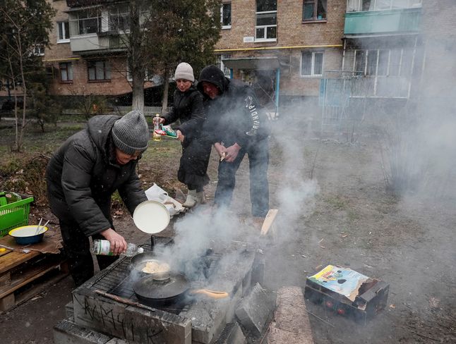 Mieszkańcy wspólnie gotują na podwórku przed blokami w Buczy.