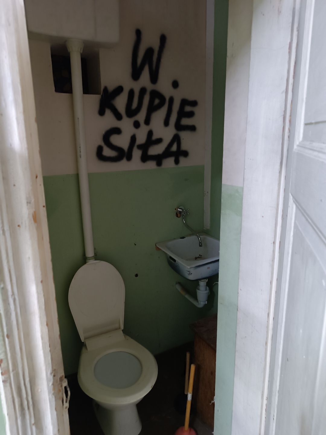 Wąska toaleta ze scenografii Świata według Kiepskich, z umywalką i napisem W kupie siła nad sedesem
