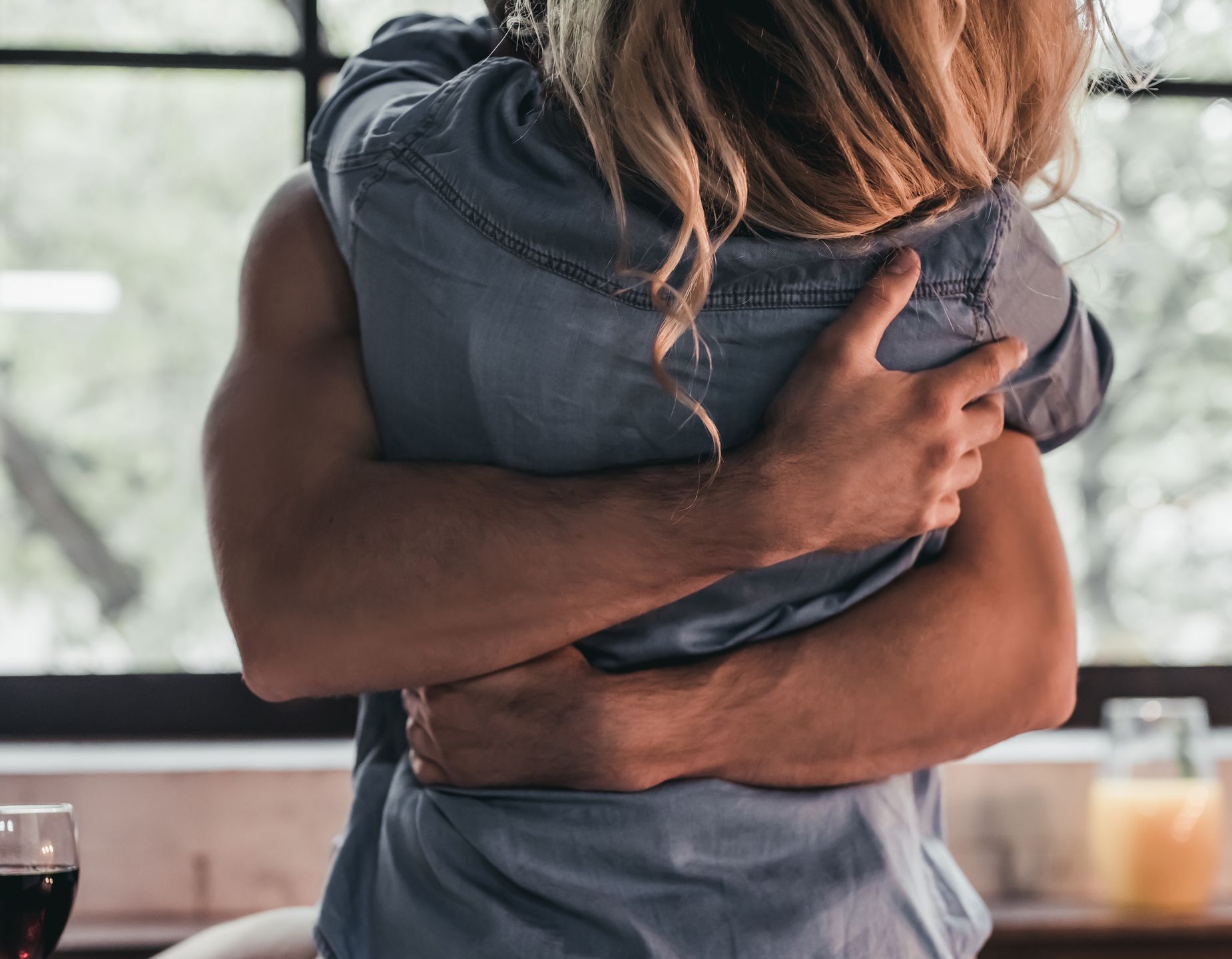 Cropped image of attractive passionate couple on kitchen. Man hugs woman while she's sitting on table.