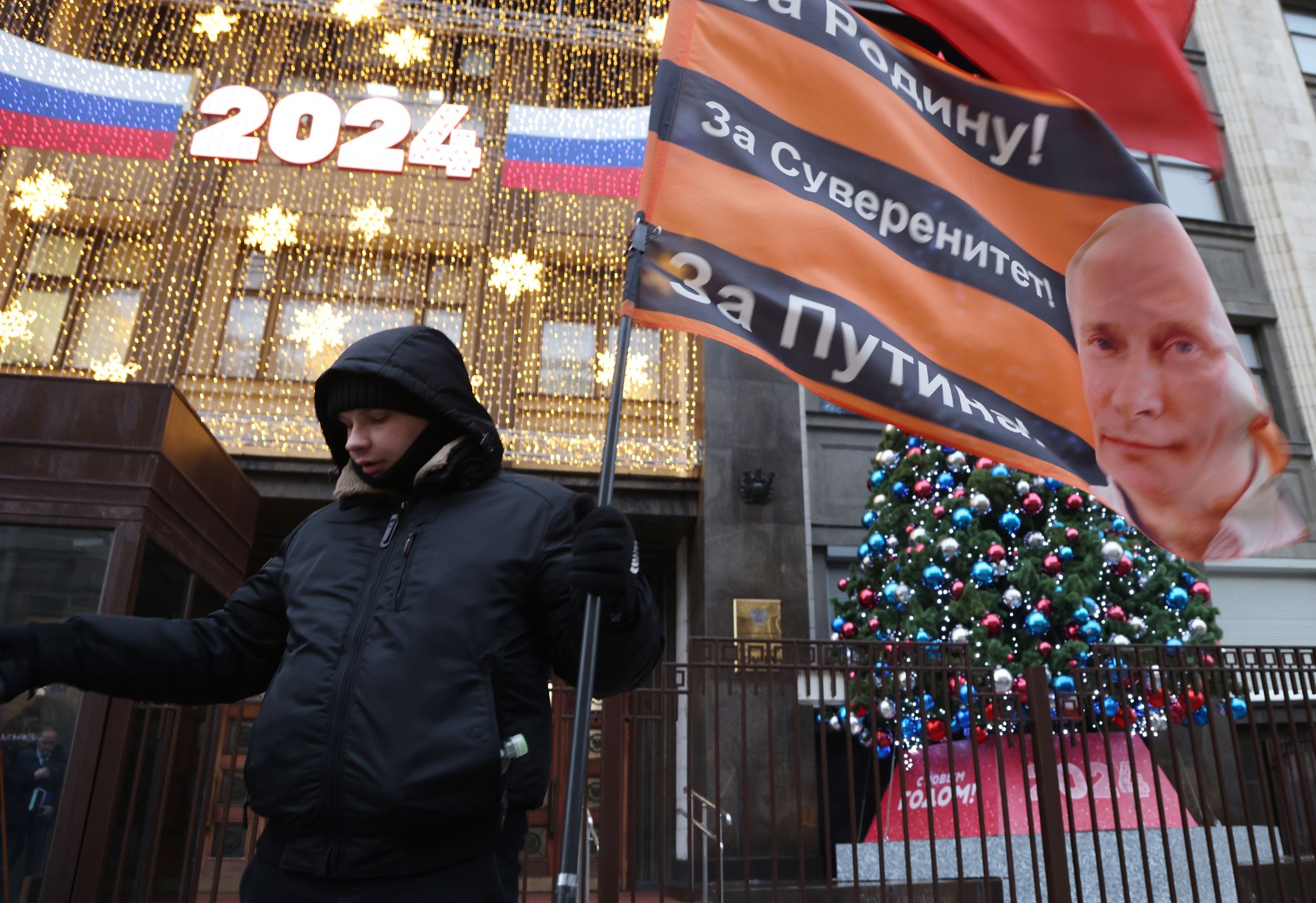 Daily Life In MoscowMOSCOW, RUSSIA - DECEMBER 19 (RUSSIA OUT) An activisit of the National Liberation Movement (NOD), a Kremlin-backed pro-Putin ogranization, holds a flag with portrait of Russian President Vladimir Putin in front of the State Duma's building, December,19, 2023, in Moscow, Russia. The sign reads: "For the Fatherland! For sovereignty! For Putin!". Vladimir Putin is nominated as candidate for the March 2024 Presidential Elections. (Photo by Contributor/Getty Images)Contributor§
