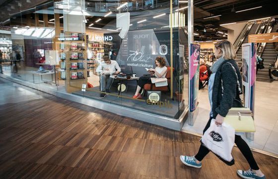 Czytający i słuchający muzyki ludzie w witrynach salonów Empik na 70-lecie sieci