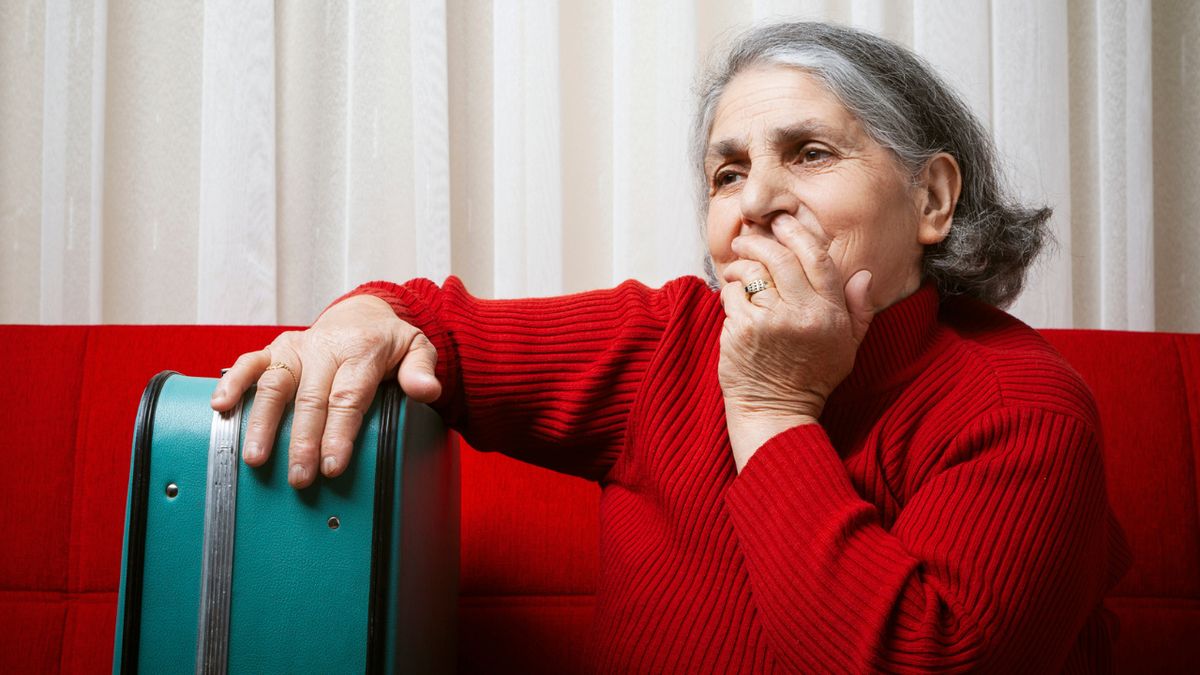 Smutna starsza kobieta ze spakowaną walizką