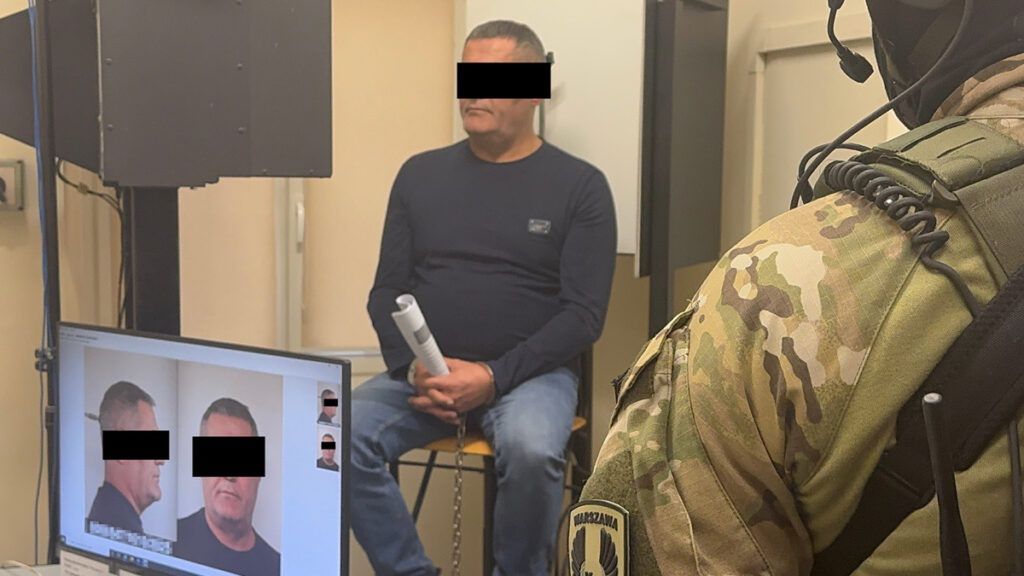 Mężczyzna siedzący na krześle w pomieszczeniu, podczas gdy na ekranie wyświetlane są jego zdjęcia.