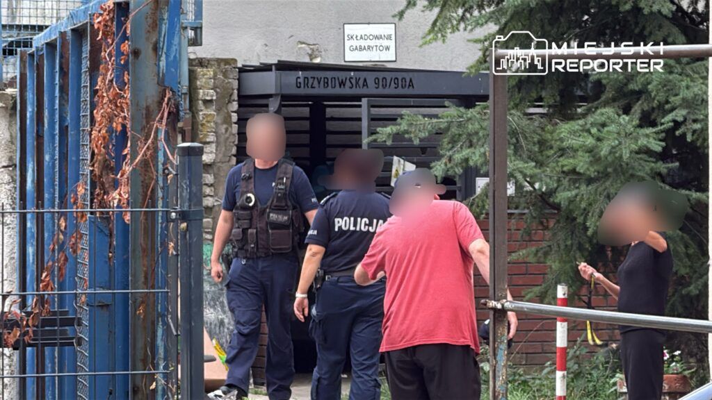 Grupa policjantów rozmawia z osobami na terenie posesji, w tle widoczny budynek z napisem "Składowanie gabarytów".
