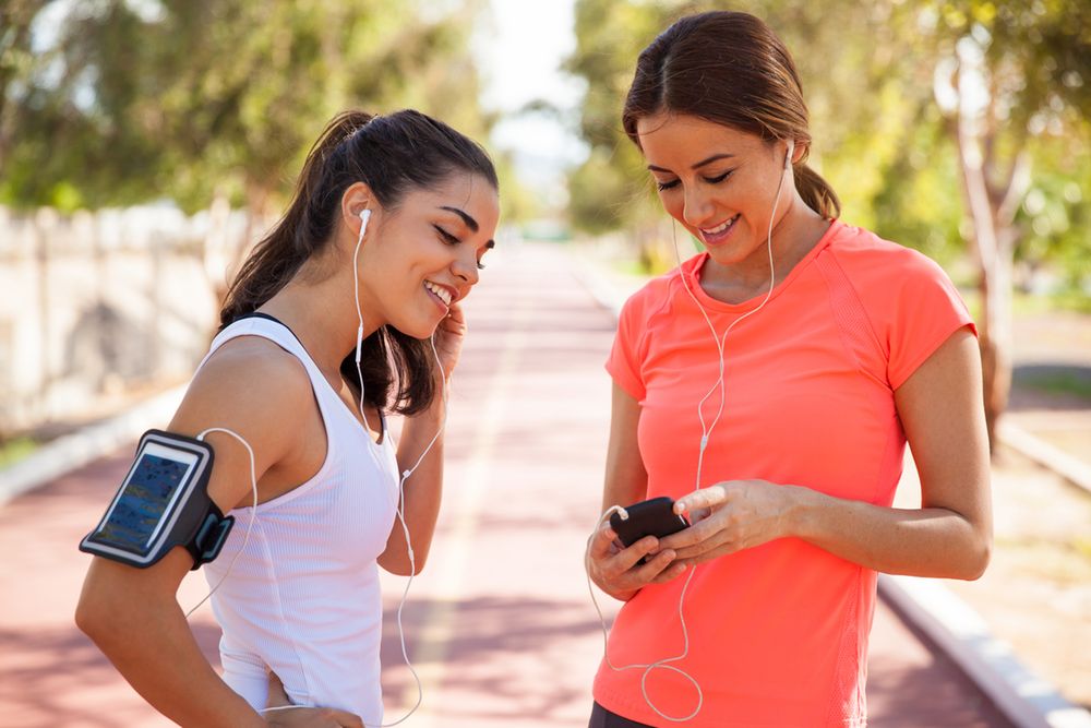Zdjęcie Cute female runners getting ready and sharing songs before going for a run pochodzi z serwisu Shutterstock