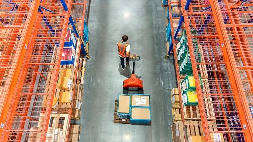 High angle view of Male warehouse worker pulling a pallet truck at distribution warehouse.Kmatta