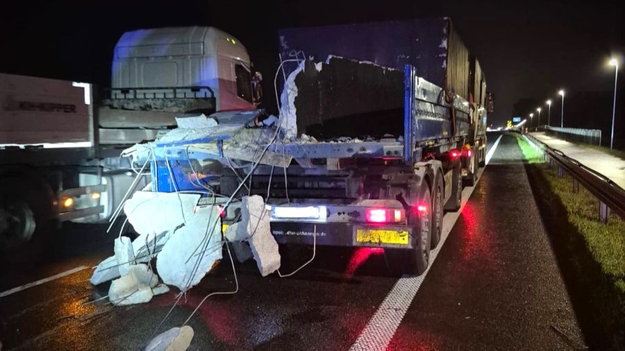 Ciężarówka z uszkodzonym ładunkiem betonowym stoi na drodze nocą, obok innych pojazdów.