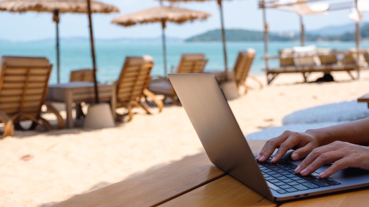 Na zdjęciu osoba na laptopie na plaży