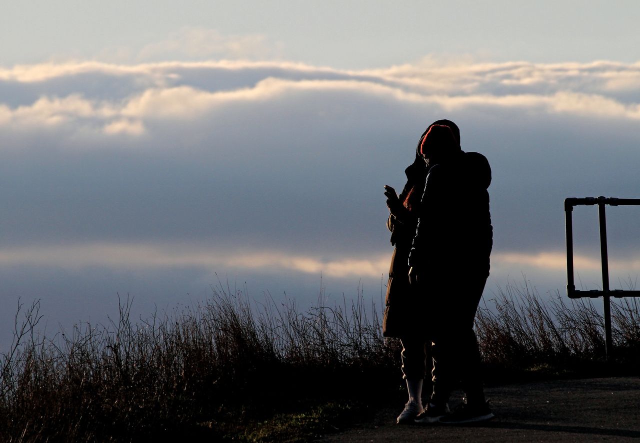 A couple is looking at photos on their mobile device as the sun sets and clouds form at the Final Approach Danville Terminal, an aviation-themed park space built on a man-made 25-meter-tall platform for viewing planes arriving and departing Toronto Pearson International Airport in Mississauga, Ontario, on March 15, 2024. (Photo by Mike Campbell/NurPhoto via Getty Images)