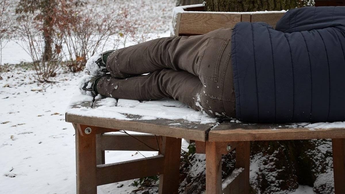 człowiek leży na ławce ze śniegiem