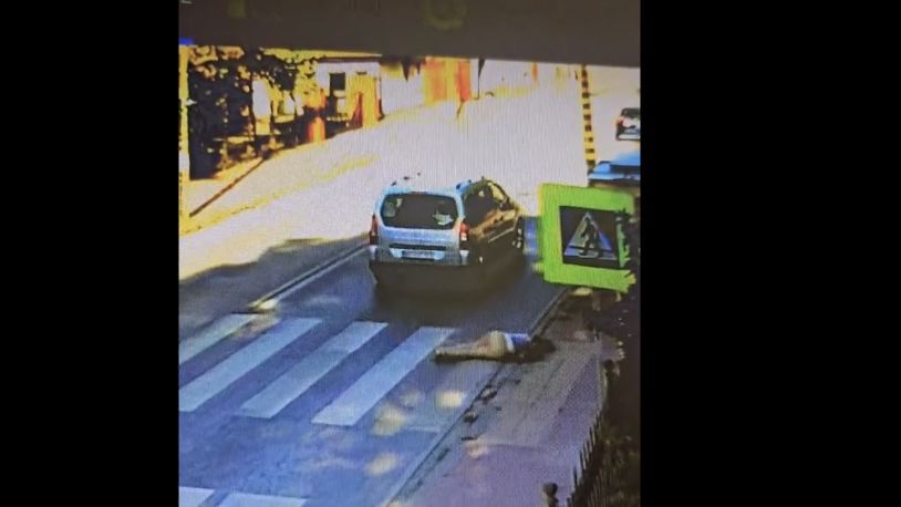 Samochód osobowy przejeżdża przez przejście dla pieszych, obok leży osoba na ziemi.